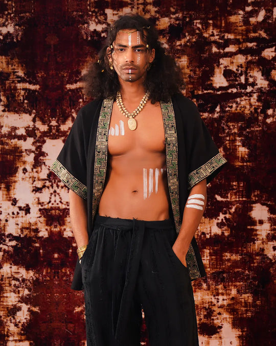 Man wearing a black robe with gold accents against a textured brown and beige background