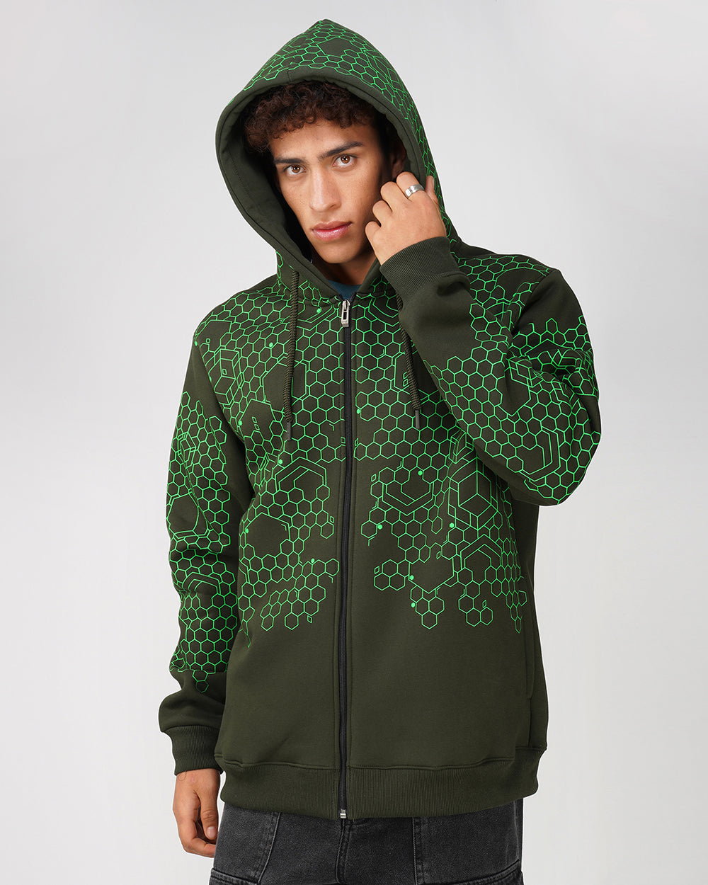 A person wearing a green zip-up hoodie with a geometric hexagon pattern, featuring a drawstring hood and ribbed cuffs.