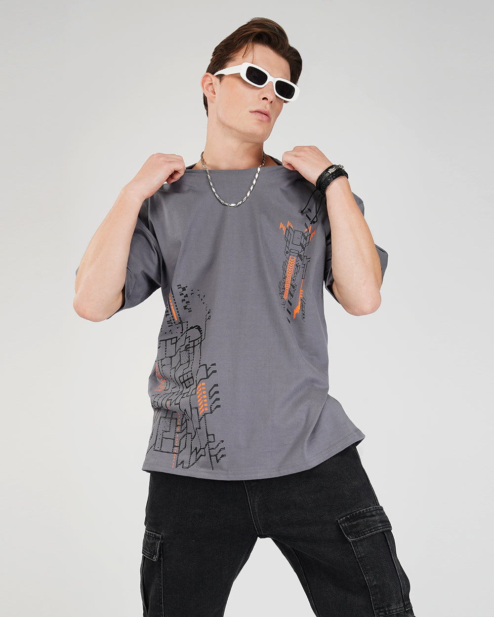 A person wearing an oversized gray cotton t-shirt with a geometric pattern, round neck, and half sleeves. The t-shirt is UV light reactive with a design that becomes visible under black light.
