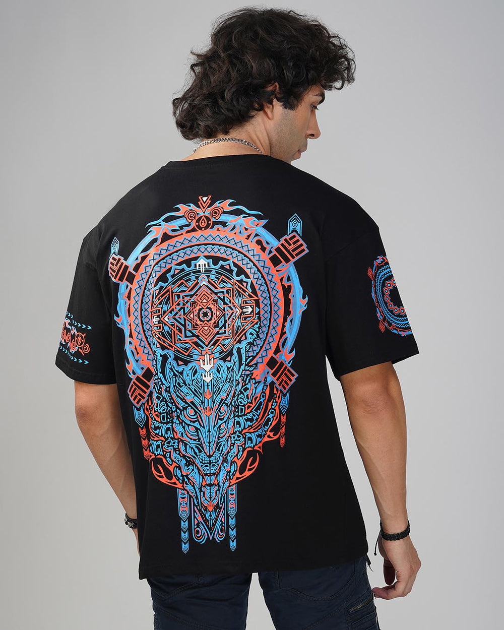 A person wearing a black oversized cotton t-shirt with a geometric and psychedelic pattern in blue and orange.