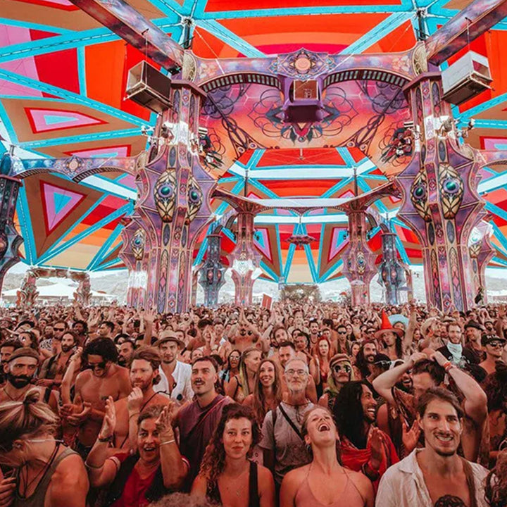 Large crowd at a music festival under a colorful geometrically designed tent.