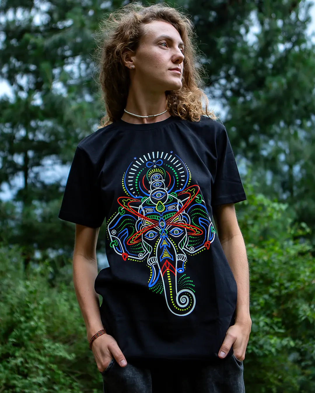 Person wearing a black t-shirt with a colorful Lord Ganesha abstract design in a forest setting