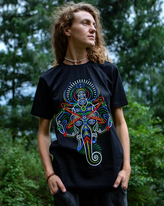 Person wearing a black t-shirt with a colorful Lord Ganesha abstract design in a forest setting