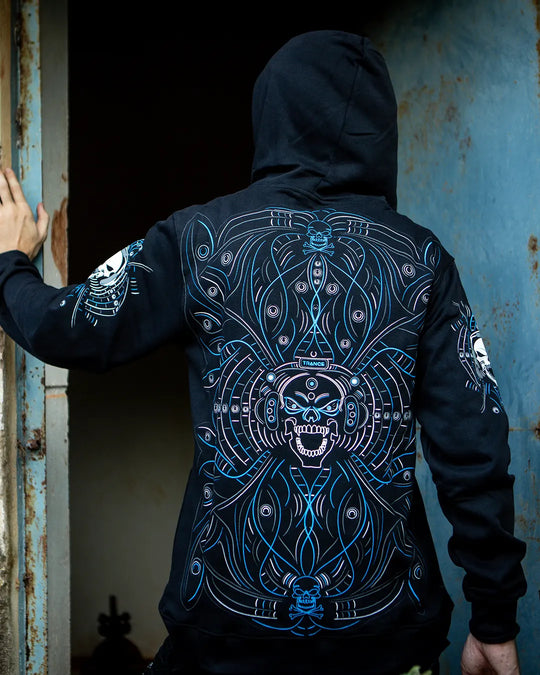 Person wearing a black hoodie with blue intricate designs on the back, standing in a dimly lit room.