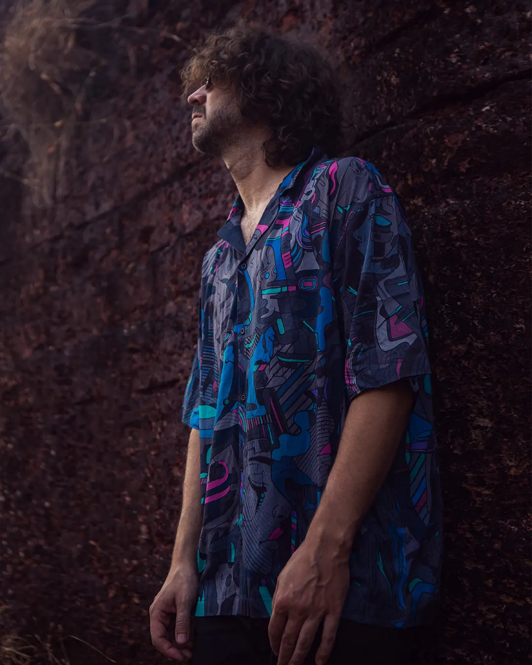 Man wearing a colorful patterned shirt against a textured brown wall