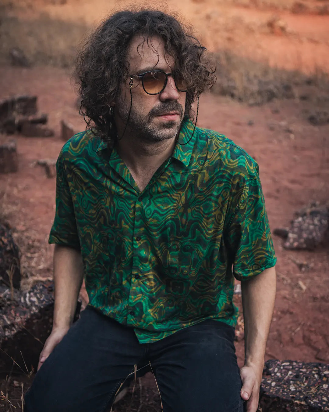 Man wearing a green patterned shirt sitting on a rocky surface