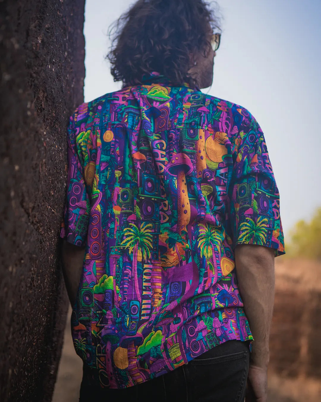 Person wearing a colorful patterned shirt leaning against a tree