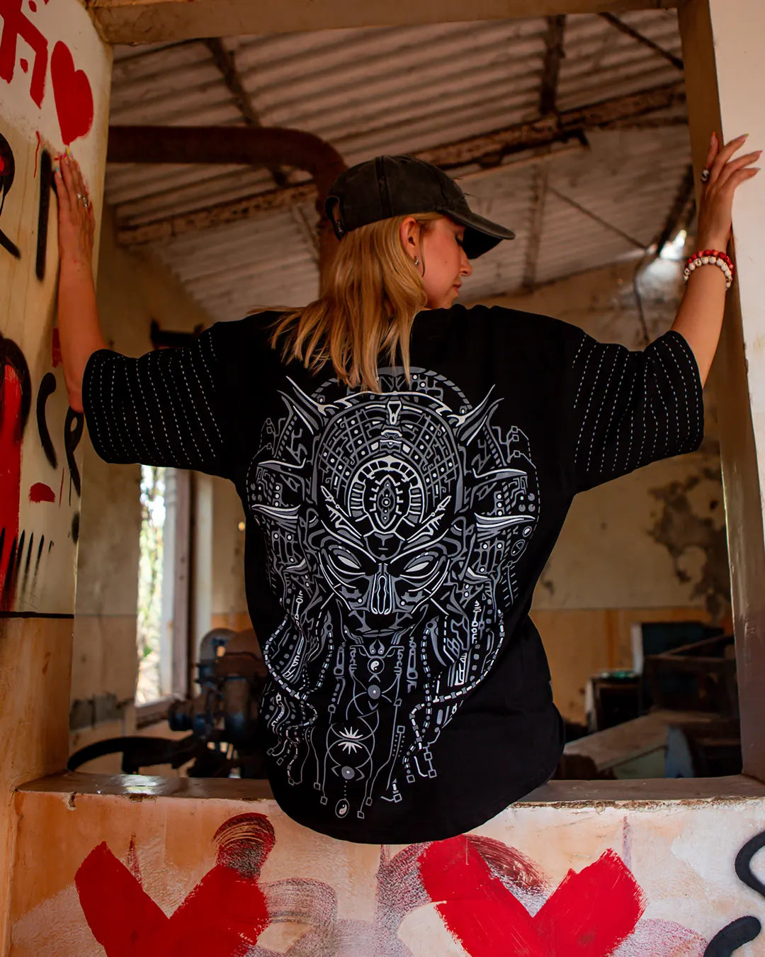 Person wearing a black shirt with a white graphic design, standing in an indoor setting with graffiti on the walls.