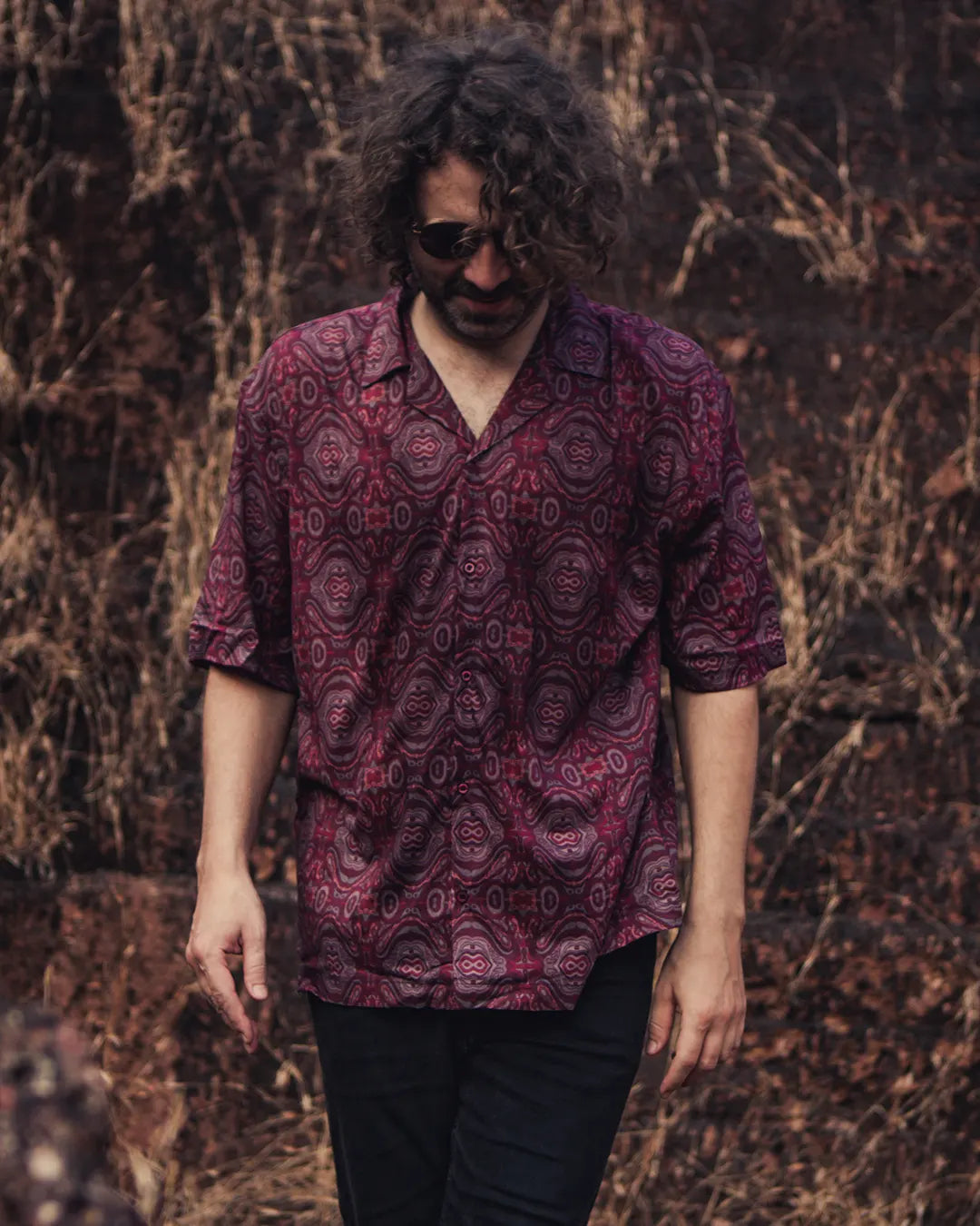 Person wearing a patterned shirt standing against a textured brown background