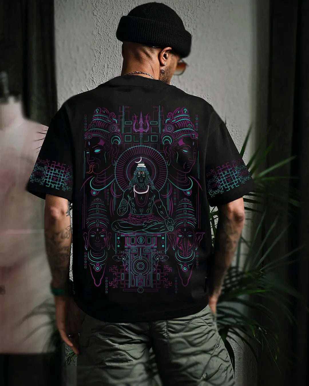 Person wearing a black t-shirt with intricate Shiva family designs on the back, standing against a neutral background.