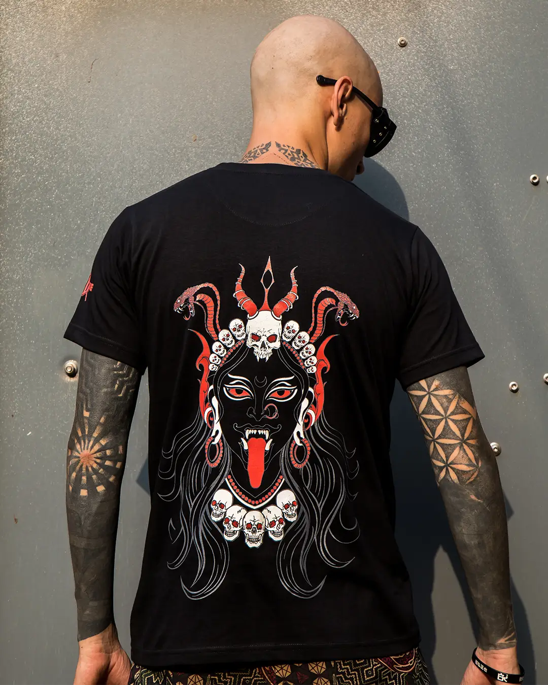 Person wearing a black t-shirt with a graphic design on the back, standing against a textured wall.