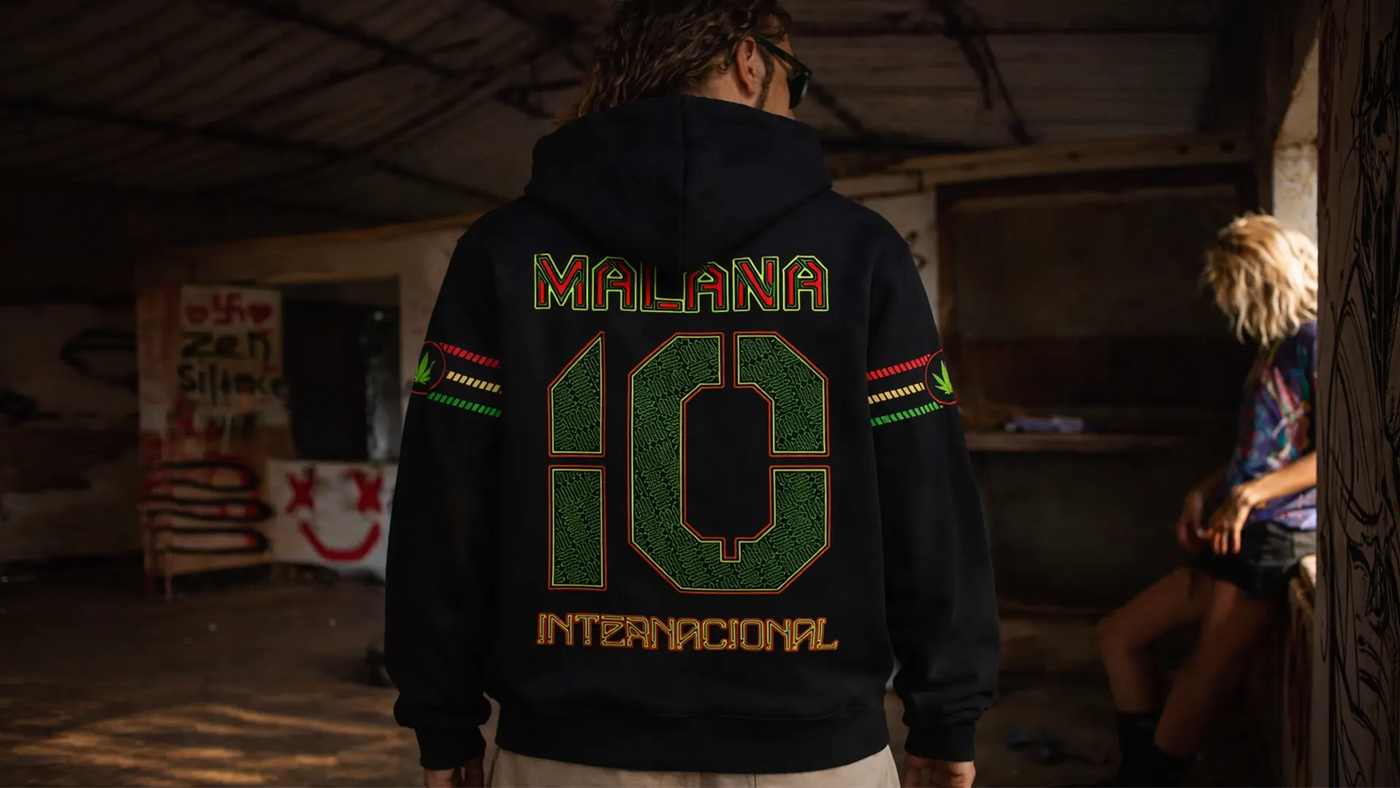 Person wearing a hoodie with 'Malana 10 Internacional' text in a dimly lit room.