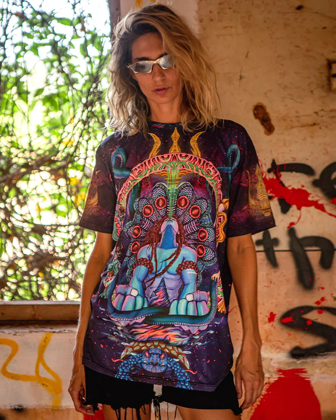 Person wearing a colorful graphic t-shirt with an elephant design in front of a graffiti-covered wall.