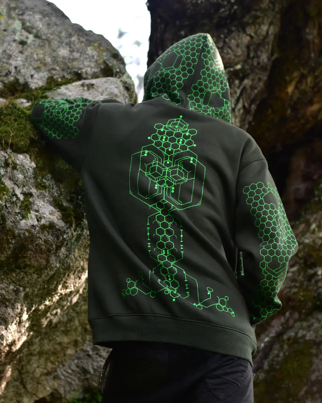 Person wearing a Dark Jungle Green hoodie with green geometric Hexagon psychedelic patterns in UV Light Reactive ink  a natural setting