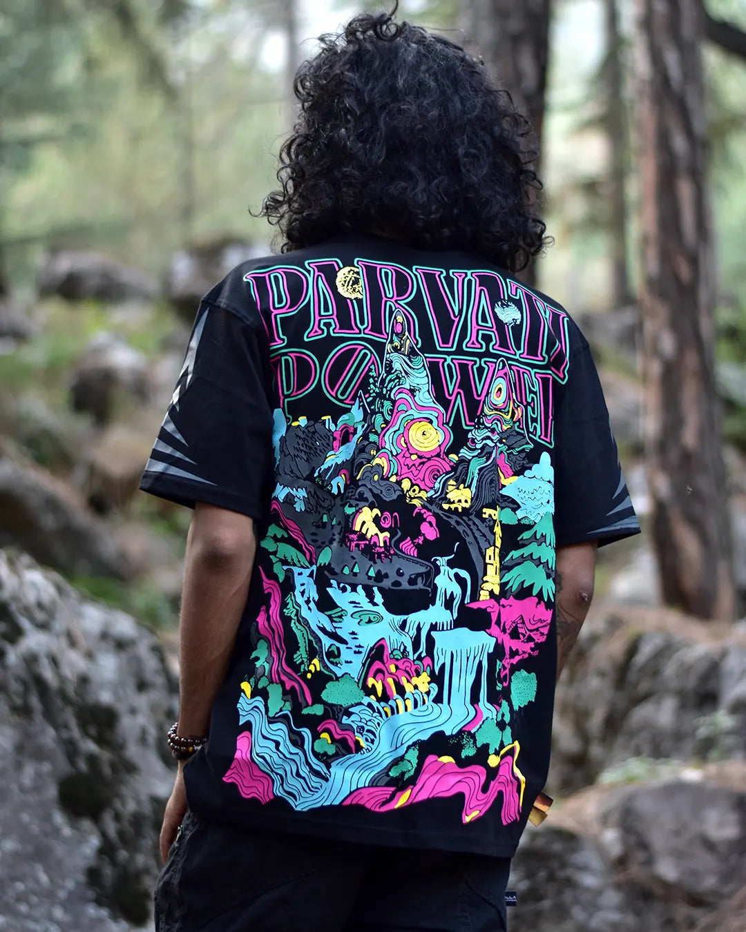 Person wearing a black t-shirt with colorful design tribute to Kasol Parvati Valley graphics Design T-Shirt by ultra tribe and text in a forest setting
