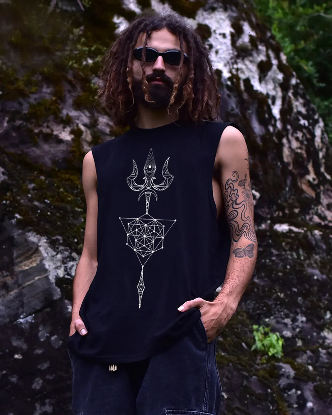 Man wearing a black sleeveless shirt with geometric design in front of a rocky background