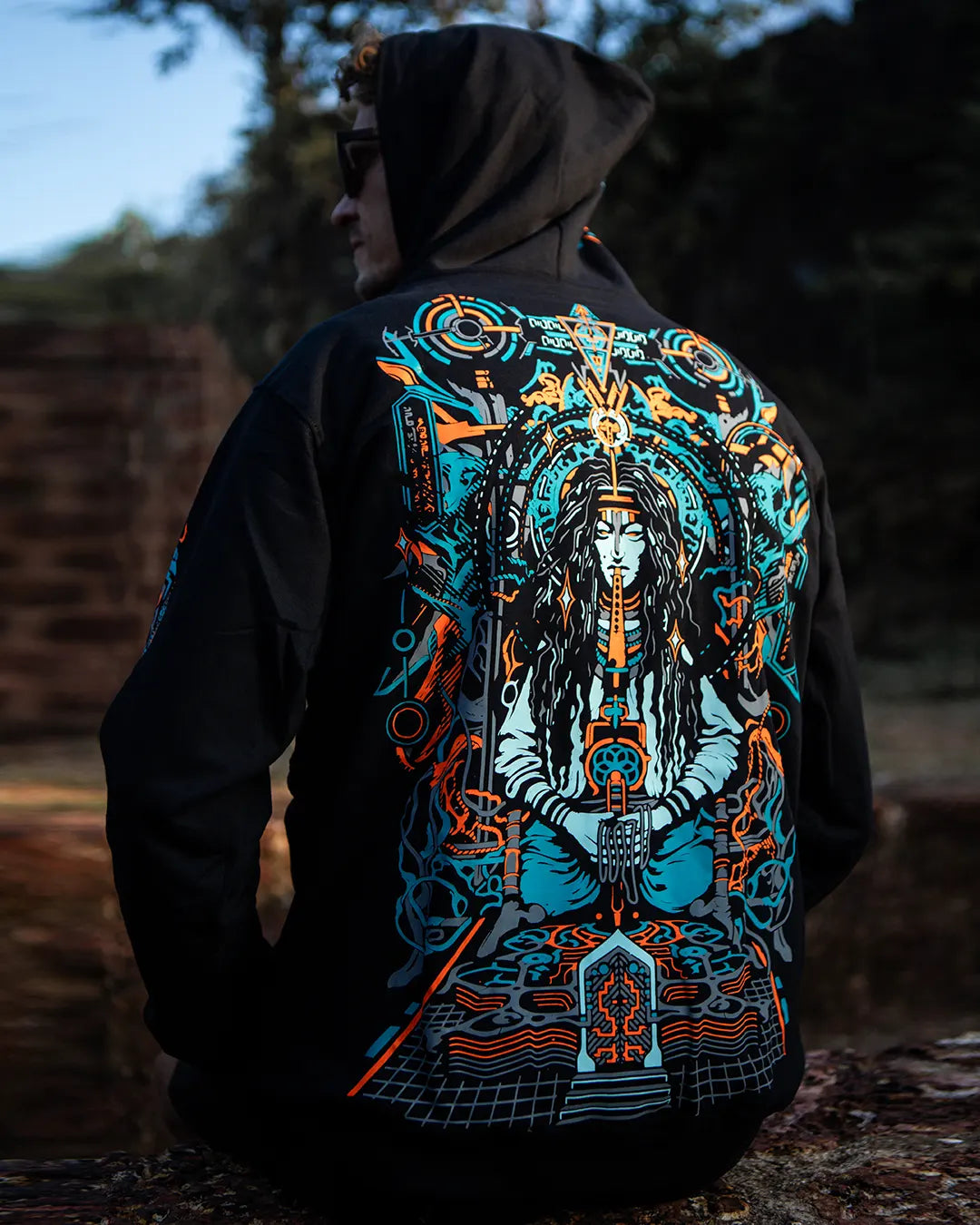 Person wearing a hoodie with a detailed design on the back, standing outdoors.