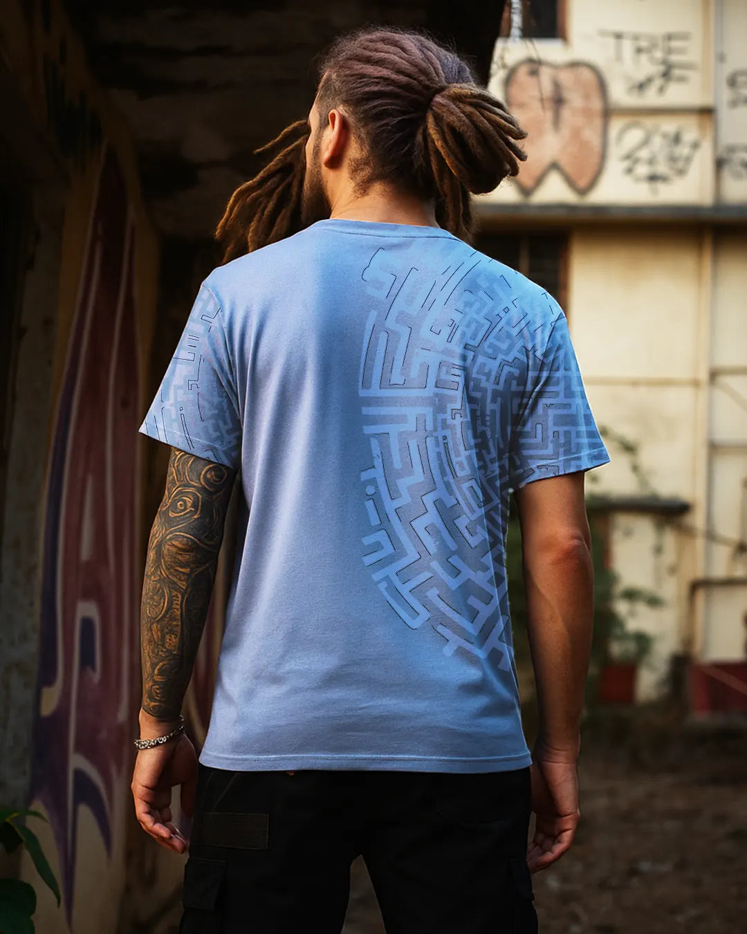 Person wearing a blue t-shirt with a geometric pattern, standing in front of a graffiti-covered wall.