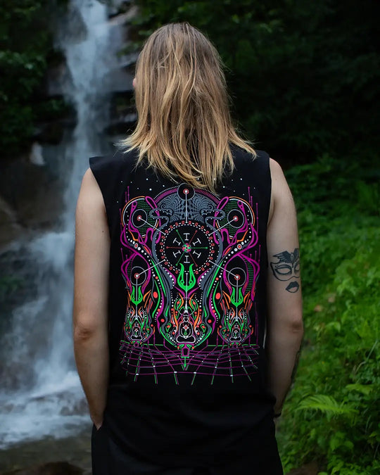 Person wearing a black sleeveless shirt with a colorful abstract design, standing in front of a waterfall.