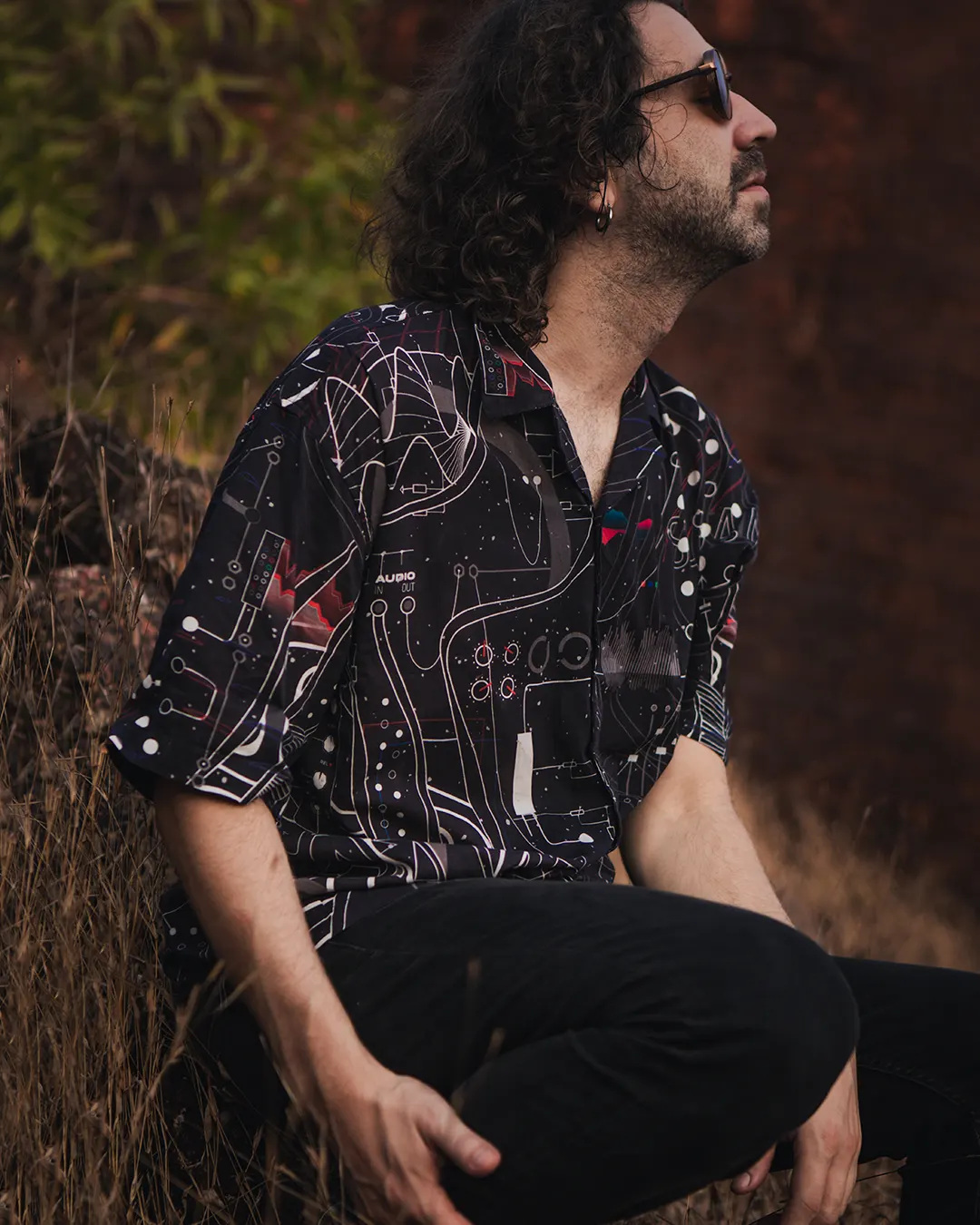 Man wearing a patterned shirt sitting outdoors with a blurred natural background
