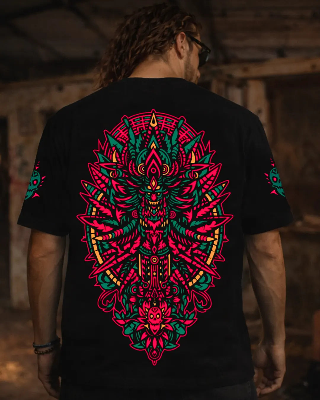 Person wearing a black t-shirt with a colorful geometric design on the back, standing in a dimly lit room.