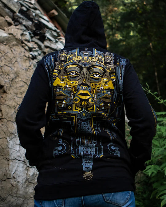 Person wearing a black hoodie with a detailed face design on the back, standing outdoors.