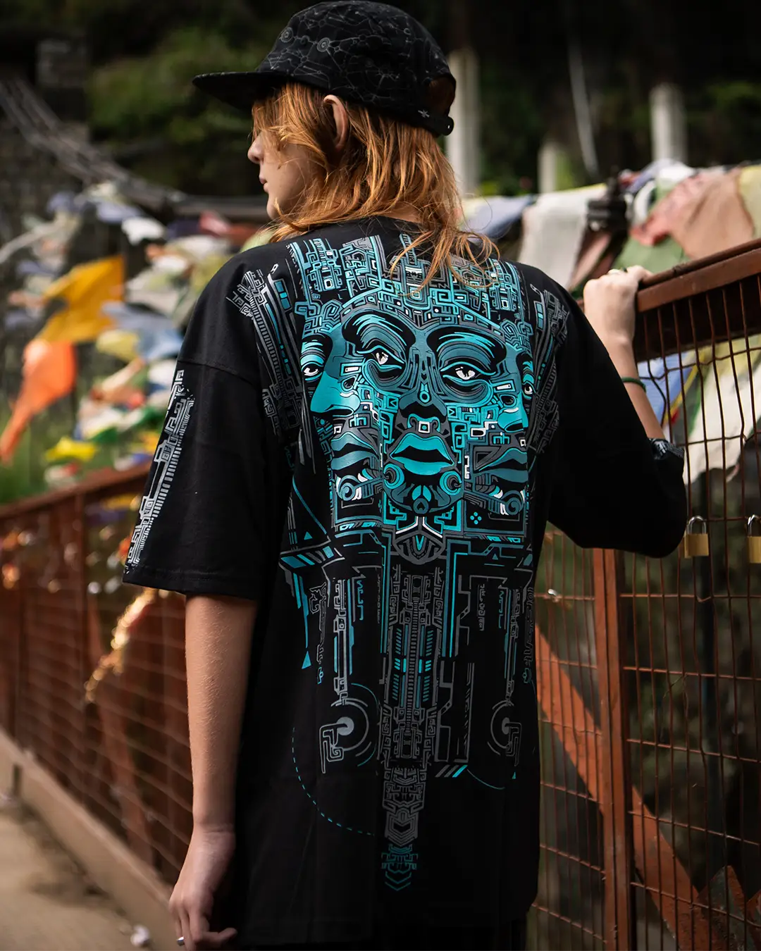 Person wearing a black t-shirt with a detailed blue design on the back, standing outdoors.
