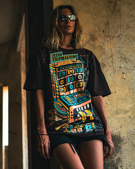 a women wearing a ultra tribe brand dark brown t-shirt with a colorful psychedleic and UV Light Reactive graphic design against a textured wall.