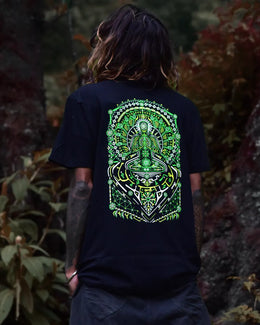 Person wearing a black uv light reactive and glow in dark t-shirt with a green and white graphic design, standing in a natural setting.