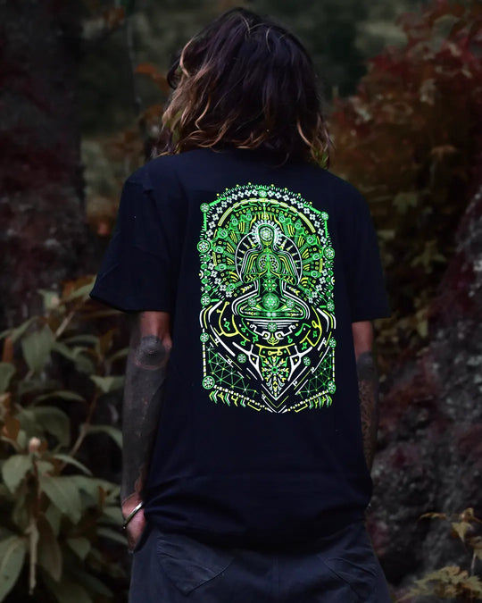 Person wearing a black uv light reactive and glow in dark t-shirt with a green and white graphic design, standing in a natural setting.