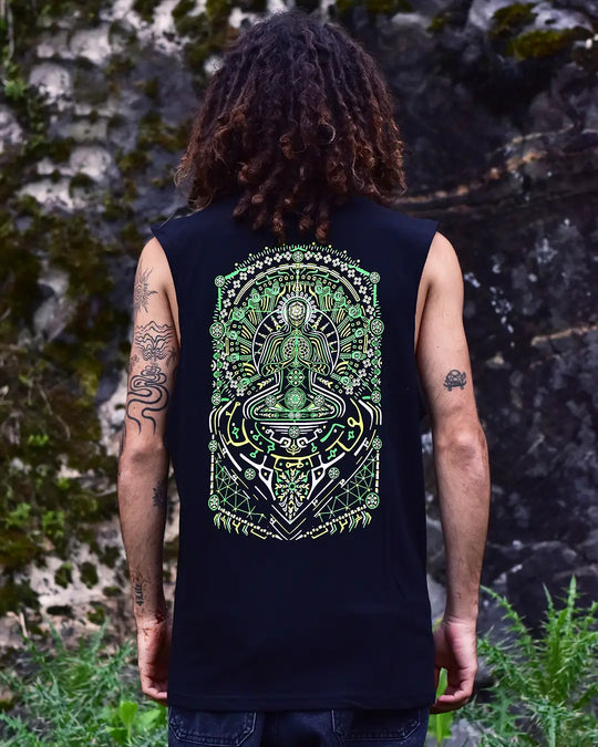 Person wearing a black sleeveless shirt with a green and white design on the back, standing against a natural stone wall.