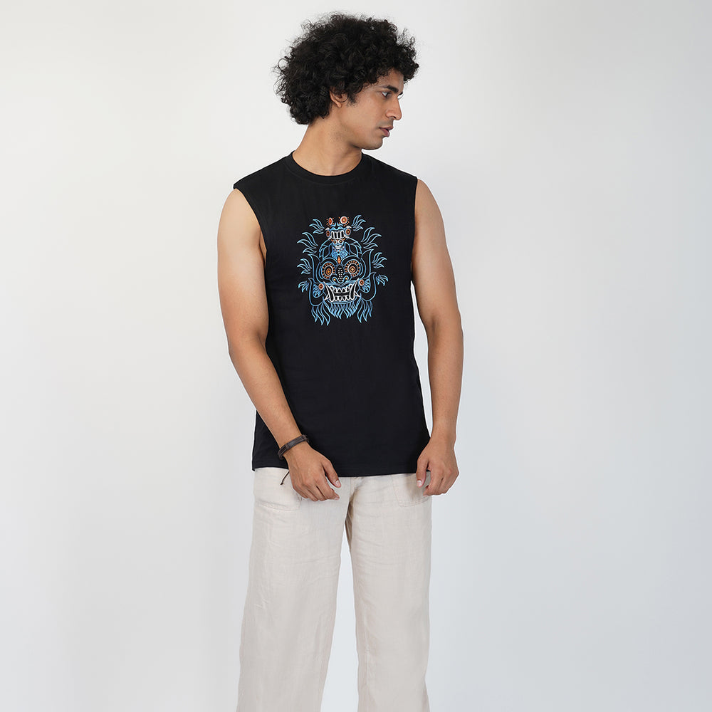 A male model wearing a black tank top with a blue and multicolor floral shaman mask print on the front.